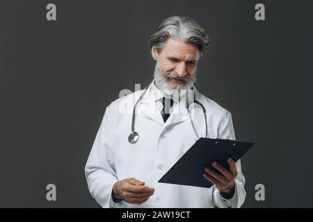 Porträt des männlichen Oberarztes mit Zwischenablage und Stethoskop auf grauem Hintergrund Stockfoto