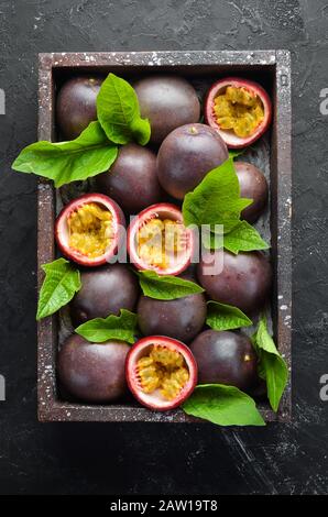 Passionsfrüchte mit Blättern auf schwarzem Hintergrund. Tropische Früchte. Draufsicht. Freier Speicherplatz für Text. Stockfoto