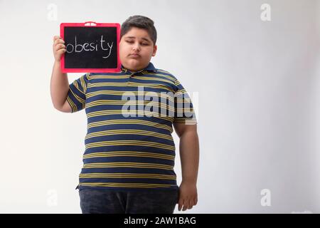 Kleiner Junge, der eine kleine Tafel mit Fettleibigkeit darauf geschrieben hat. Stockfoto