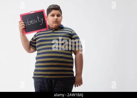 Kleiner Junge, der eine kleine Tafel mit Fettleibigkeit darauf geschrieben hat. Stockfoto