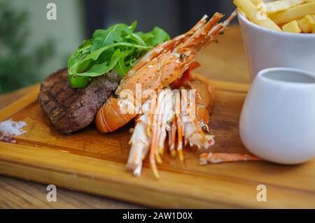 Vom Rasen gegrillter Hummersteak mit pommes frites auf Holztablett Stockfoto