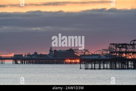 Brighton UK 6. Februar 2020 - Die Sonne steigt hinter Brightons zwei Piers an einem kalten hellen Morgen auf. Für die nächsten paar Tage wird in Großbritannien ein noch feineres Wetter prognostiziert, bevor das stürmische Wetter am Wochenende eintreffen wird. Kredit: Simon Dack / Alamy Live News