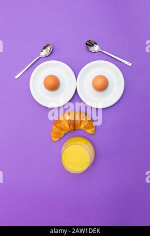 Lustiges Frühstückskonzept mit abstraktem, staunenden menschlichen Gesicht aus Frühstücksartikeln im violetten Hintergrund Stockfoto