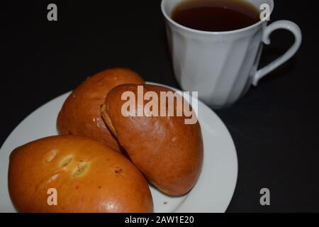 Drei Pasteten auf einem weißen Teller und eine Tasse Kaffee auf schwarzem Hintergrund. Nahaufnahme Stockfoto