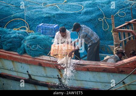 DIU, Indien - Dezember 2018: Fischer schütten das überschüssige Eis von Booten, die mit blauen Fischernetzen bedeckt sind, ins Meer. Stockfoto