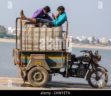 DIU, Indien - Dezember 2018: Zwei Fischer entspannen sich auf den Eiskästen, die auf einem Dreiradfahrzeug von einem Pier auf der Insel Diu beladen sind. Stockfoto