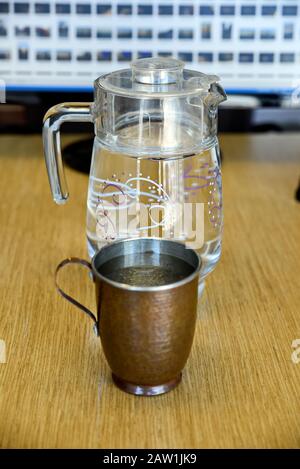 Echte und reine Kupferbecher mit Glaskrug aus Wasser auf dem Tisch im Büro Stockfoto