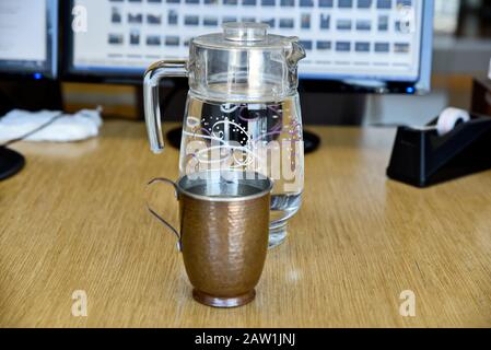 Echte und reine Kupferbecher mit Glaskrug aus Wasser auf dem Tisch im Büro Stockfoto