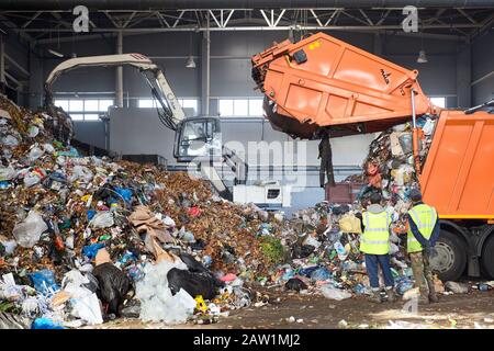 Grodno, WEISSRUSSLAND - OKTOBER 2018: Zwei Arbeiter der Recycling-Anlagensteuerung, die Müll aus Müllwagen entladen. Manipulator lädt Müll auf c Stockfoto