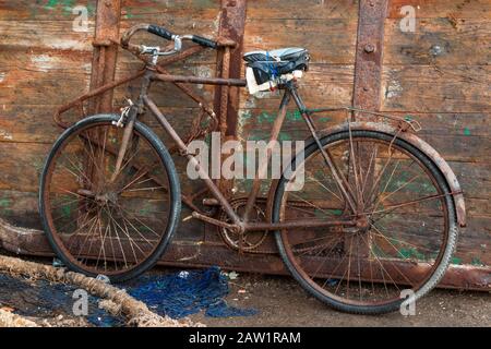 Altes Fahrrad, mit allen Teilen verrostet, aber immer noch benutzt. Holztür im Hintergrund. Fischnetz im Vordergrund. Hafen von Essaouira, Marokko. Stockfoto