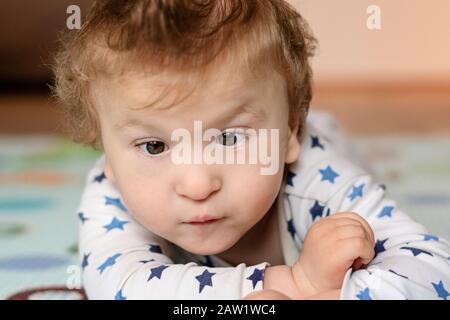 Porträt eines Babys mit zerebraler Lähmung auf dem Bauch liegend und zu Hause spielend. Spezielle Bedürfnisse Kind. Nahaufnahme behinderter Babyjungen. Stockfoto