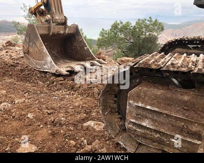 Baggerschaufel reduziert den Boden beim Straßenbau auf den steinigen Böden. Schwere Maschinen bei Erd-, Graben- und Grabungsarbeiten. Stockfoto