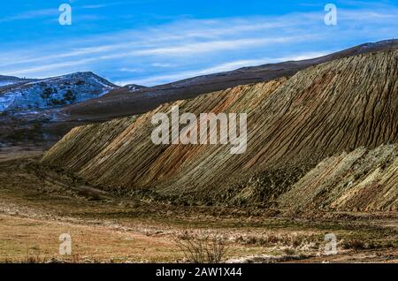 Berglandschaft mit einem melierten Hang eines Hügels, der sich von Wind und Feuchtigkeit bewegt, mit Sand und kleinem Stein aus einem verlassenen Steinbruch in Arm bestreut Stockfoto