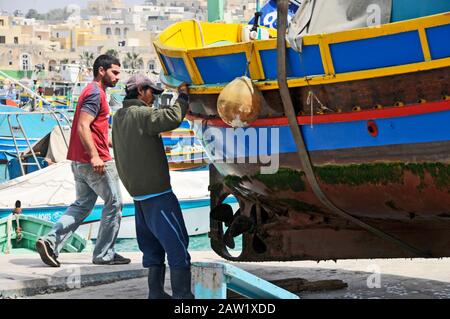 Um Malta herum - Männer, die an einem Luzzu arbeiten, außer Wasser., Marsaxlokk Stockfoto