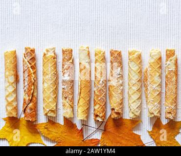 Hausgemachter Kuchen. Köstliche Waffelrollen mit Puderzucker auf einer strukturierten Serviette mit trockenen Herbstblättern. Süßer gebackener Snack für den Urlaub, Blick von oben Stockfoto