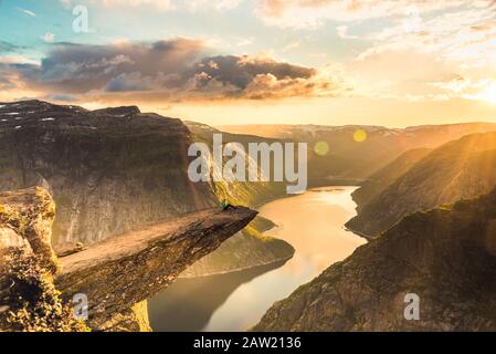 02/09-17, Trolltunga, Norwegen. Eine Frau sitzt am Rand der Trolltunga, die der Sonne zugewandt ist. Die Fallenlegung beträgt 700 m. Stockfoto