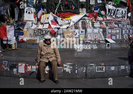 Mann sitzt auf Stufen der Marianne-Statue vor den Nachrichten, die an Opfer von Anschlägen in Paris und Brüssel erinnern, Place de la République, Paris, Frankreich - April 2016 Stockfoto