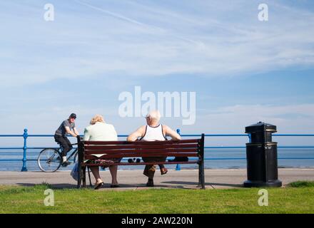 Rückansicht eines älteren Ehepaares auf dem Sitz mit Blick auf den Strand. GROSSBRITANNIEN Stockfoto