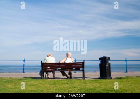 Rückansicht eines älteren Ehepaares auf dem Sitz mit Blick auf den Strand. GROSSBRITANNIEN Stockfoto