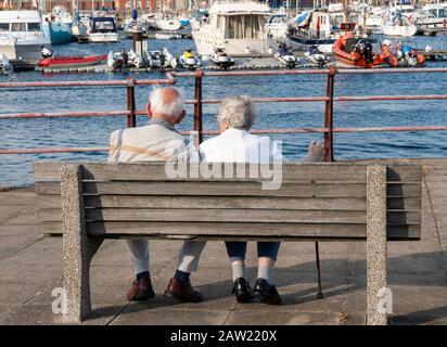 Rückansicht eines älteren Ehepaares auf dem Sitz mit Blick auf den Strand. GROSSBRITANNIEN Stockfoto