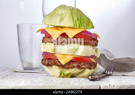 Burger ohne Salat, glutenfrei, mit Gemüse, Hacksteaks und Käse. Auf Holzgrund. Neben Glaskügeln. Stockfoto