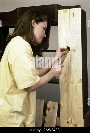 Frau, die einen Nagel in eine Holzplanke hämmert Stockfoto