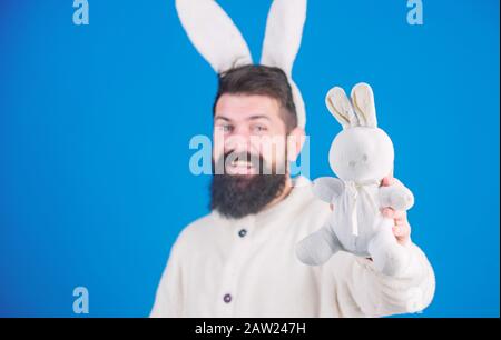 Konzept des Ostersymbols. Kerl bärtiger Flusspferd süßer sanfter, bunter langer Ohren blauer Hintergrund. Osterhase. Respekt vor Traditionen. Mann mit buntweichem Plüsch Stockfoto