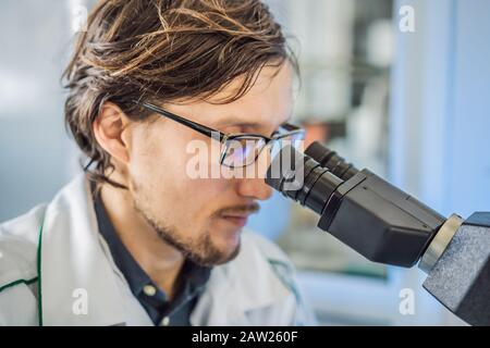 Porträt des wissenschaftlichen Forschers des kaukasischen männlichen Chemikers mit Mikroskop im Inneren des Labors Coronavirus Stockfoto