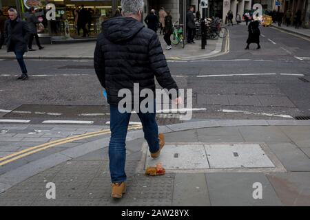 Fußgänger vermeiden einen Nudel- und Sauce-Mitnahme, fallen gelassen und während der Mittagsstunde im Finanzviertel der Hauptstadt am 4. Februar 2020 in der City of London, England, auf dem Straßenbelag entsorgt. Die Mittagsmahlzeit wurde auf der Straße getragen, als ihre Hitze und Feuchtigkeit es durch den Boden einer Papiertüte fallen ließen, sie umgedreht und perfekt auf dem Straßenbelag liegend, als die Stadtarbeiter aus ihren Büros auftauchten. Diejenigen, die es rechtzeitig sahen, traten über das schmierige Hindernis, aber die ablenkten (meist durch das gehen mit Telefonen zu Ohren), traten in es und halfen, es über den Straßenbelag zu verbreiten. Stockfoto