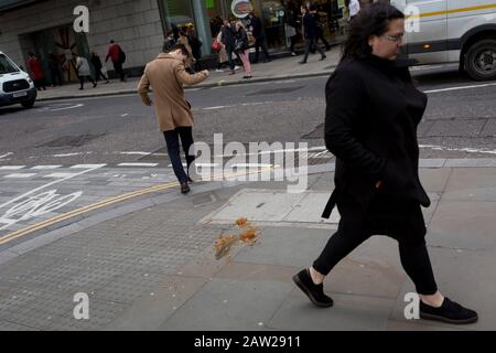 Ein Fußgänger vermeidet es nicht, eine Nudel und Sauce zu nehmen, die während der Mittagsstunde im Finanzviertel der Hauptstadt, am 4. Februar 2020, in der Stadt London, England, auf dem Straßenbelag abgeworfen und verworfen wurden. Die Mittagsmahlzeit wurde auf der Straße getragen, als ihre Hitze und Feuchtigkeit es durch den Boden einer Papiertüte fallen ließen, sie umgedreht und perfekt auf dem Straßenbelag liegend, als die Stadtarbeiter aus ihren Büros auftauchten. Diejenigen, die es rechtzeitig sahen, traten über das schmierige Hindernis, aber die abgelenkt (meist durch gehen mit Telefonen zu Ohren), traten in es und halfen, es über das zu verbreiten Stockfoto