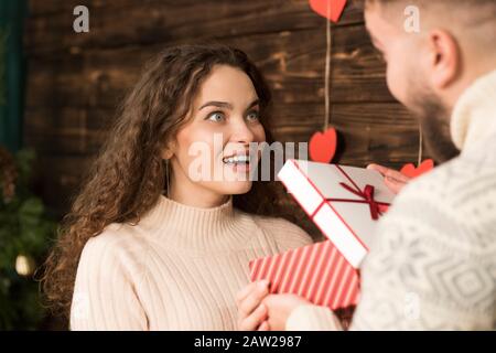 3/4-Ansicht des Mannes, der der lachenden Freundin am valentinstag ein Geschenk präsentiert. Stockfoto