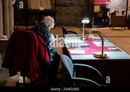 Eine ältere Dame, die an einem Schreibtisch sitzt und unter Lampenlicht liest Stockfoto