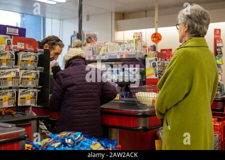 Käufer stehen an der Kasse eines Supermarktes Schlange und legen Produkte auf das Förderband Stockfoto