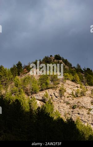 Der kontrastreiche Blick auf die niedrigen französischen Alpen unter warmem Sonnenlicht vor dem Hintergrund des trüben dunklen Himmels Stockfoto