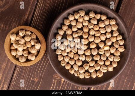 Viel frische Kichererbse in glasierter Schüssel in Bambusschale auf braunem Holz flatlay Stockfoto