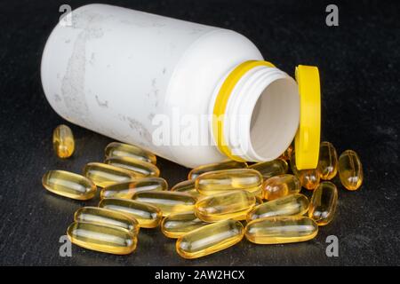 Viel goldenes Fischöl mit weißer Plastikflasche auf grauem Stein Stockfoto