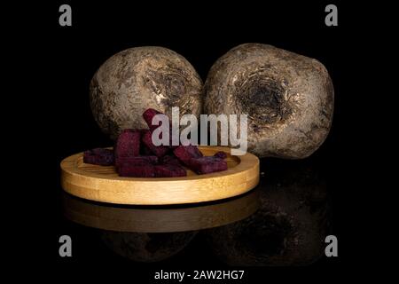 Gruppe von zwei ganzen Stücken roher süßer Bete auf runder Bambusbahn isoliert auf schwarzem Glas Stockfoto
