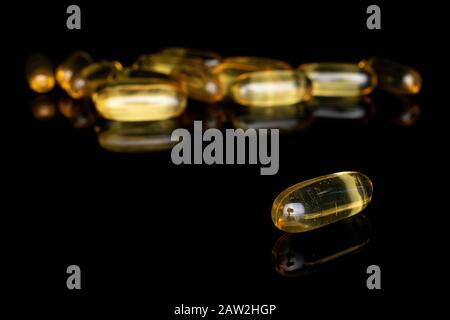 Viel ganz ungeordnetes goldenes Fischöl isoliert auf schwarzem Glas Stockfoto