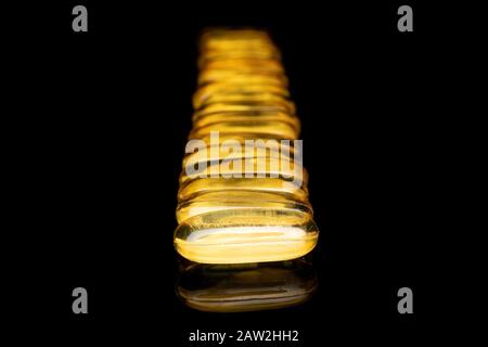 Auf schwarzem Glas isoliert, viele ganze goldene Fischölkapsel Stockfoto