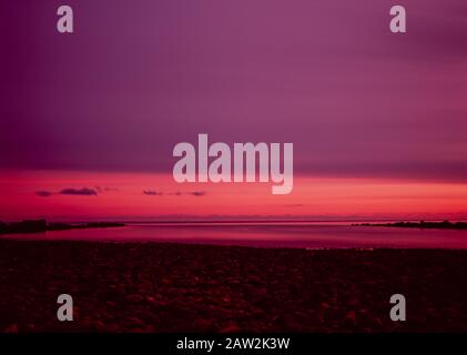 Ein rosafarbener Sonnenaufgang und purpurer Himmel Über EINEM roten Strand Stockfoto