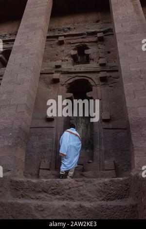 Lalibela, Äthiopien - November 2018: Mann in weiße traditionelle äthiopische Kleidung gekleidet, die an der ausgegrabenen Felsenkirchenkirche in Lalibela bettet. Stockfoto