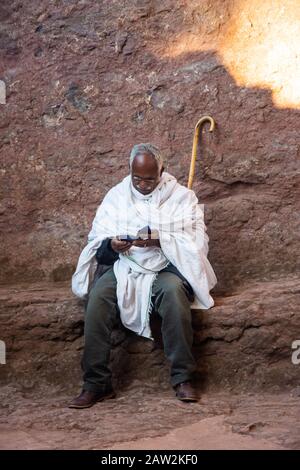 Lalibela, Äthiopien - November 2018: Mann kleidete sich traditionelles Weiß, saß draußen und las ein Gebetbuch neben den unterirdischen Kirchen von Lalibela Stockfoto