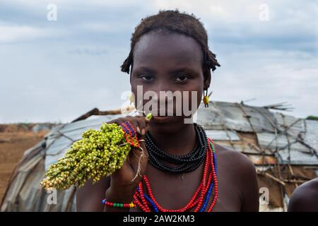 Omorate, Äthiopien - Nov 2018: Dasanech-Stammfrau kaut Sorghum vor dem Stammeshaus. Omo-Tal Stockfoto