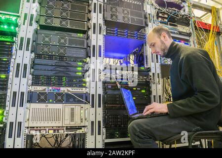 Der diensthabende Techniker mit dem Laptop arbeitet im Serverraum. Der Programmierer, der den Computer auf seinem Schoß hat, befindet sich im Rechenzentrum. Konzept der Information Stockfoto