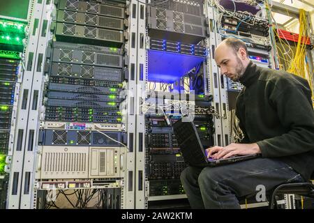 Ein Mann mit Laptop sitzt im Serverraum des Rechenzentrums. Der Systemadministrator arbeitet in der Nähe der Racks mit den Servern. Computeringenieur Stockfoto
