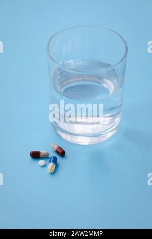 Tabletten und Pillen auf blauem Hintergrund mit einem Glas Wasser, Medikamentenkonzept, Kopierraum, selektivem Fokus Stockfoto