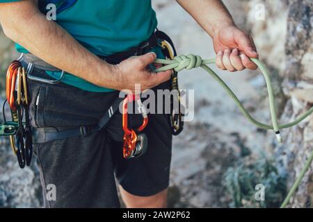 Nahaufnahme des Kletterers mit Kletterausrüstung, Knotenbindung am Klettergurt, Vorbereitung zum Klettern. Stockfoto
