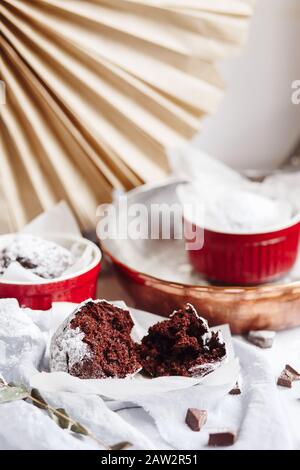 Schokoladenmuffins in roten Tassen. Kleines glasiertes Keramikramekin mit braunen Kuchen auf grauem und weißem Grund Stockfoto