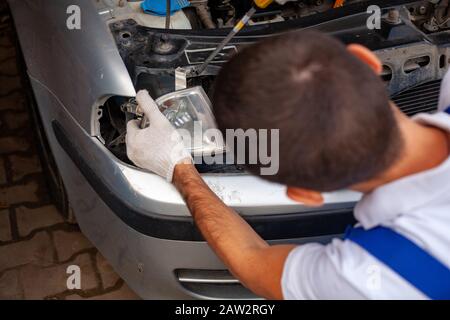 Mechaniker mit Schraubenschlüssel reparieren den Motor in der Werkstatt - Autoservice, Reparatur, Wartung und Personenkonzept. Der Meister repariert den Scheinwerfer des Wagens und entfernt die Beleuchtung Stockfoto