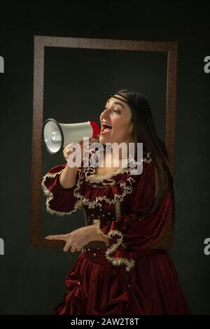 Verkaufsabruf. Porträt der mittelalterlichen jungen Frau in roter Vintage-Kleidung, die auf dunklem Hintergrund steht. Weibliches Modell als Herzogin, königliche Person. Gegenüberstellung von Epochen, Moderne, Mode, Schönheit. Stockfoto